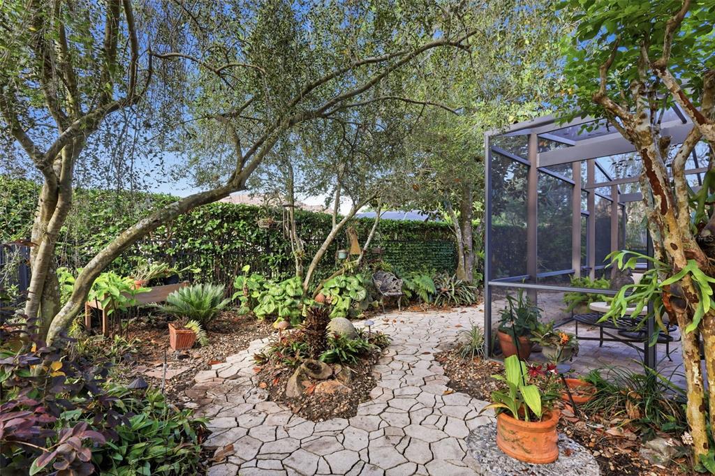 A stone pathway leads through a lush garden toward a screened-in patio area — 1609 VICTORIA GARDENS DRIVE, DELAND, FL