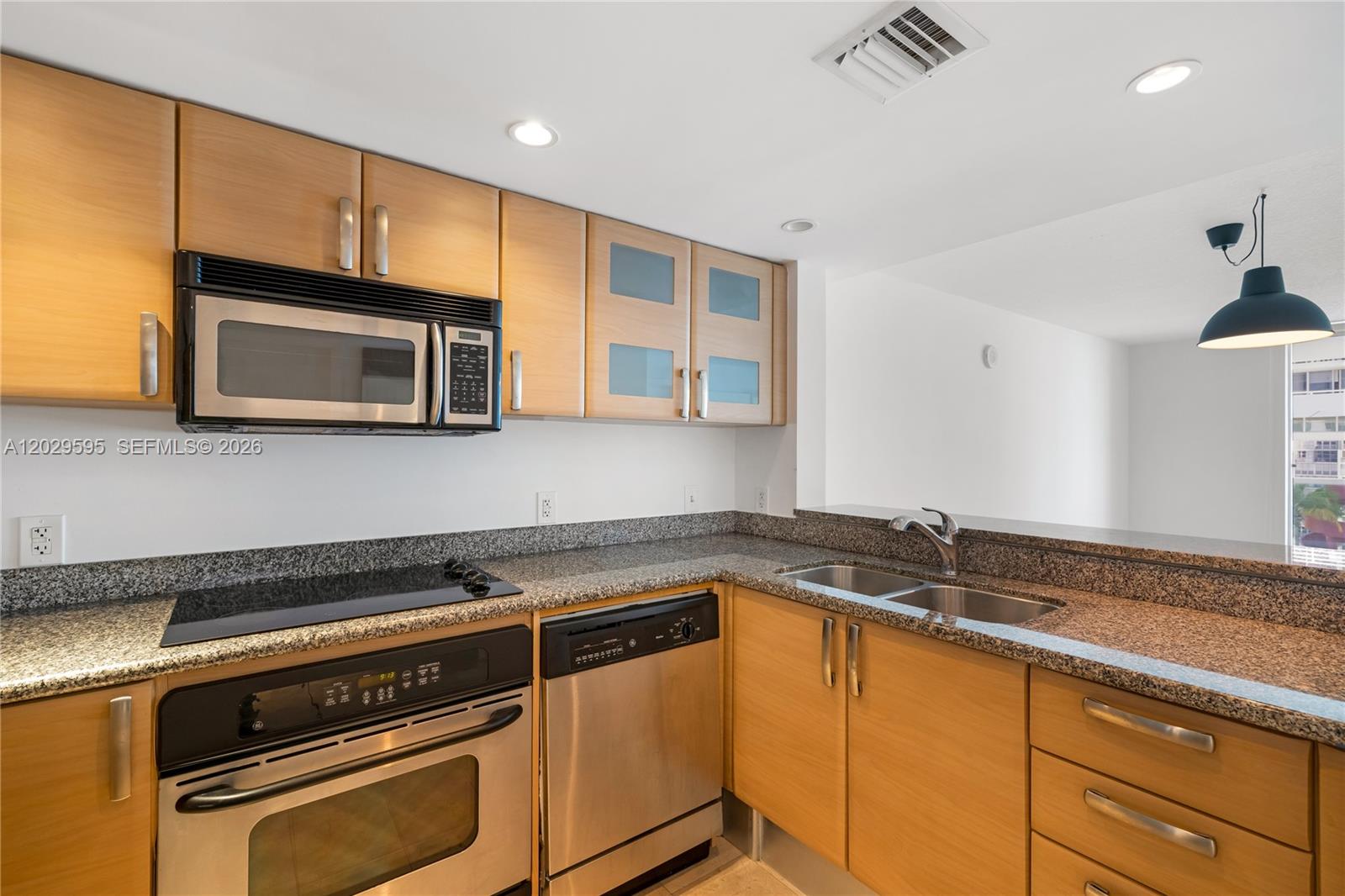 A kitchen features light wood cabinets, granite countertops, and stainless steel appliances — 2101 Brickell Ave # 1103, Miami FL 33129, MIAMI, FL