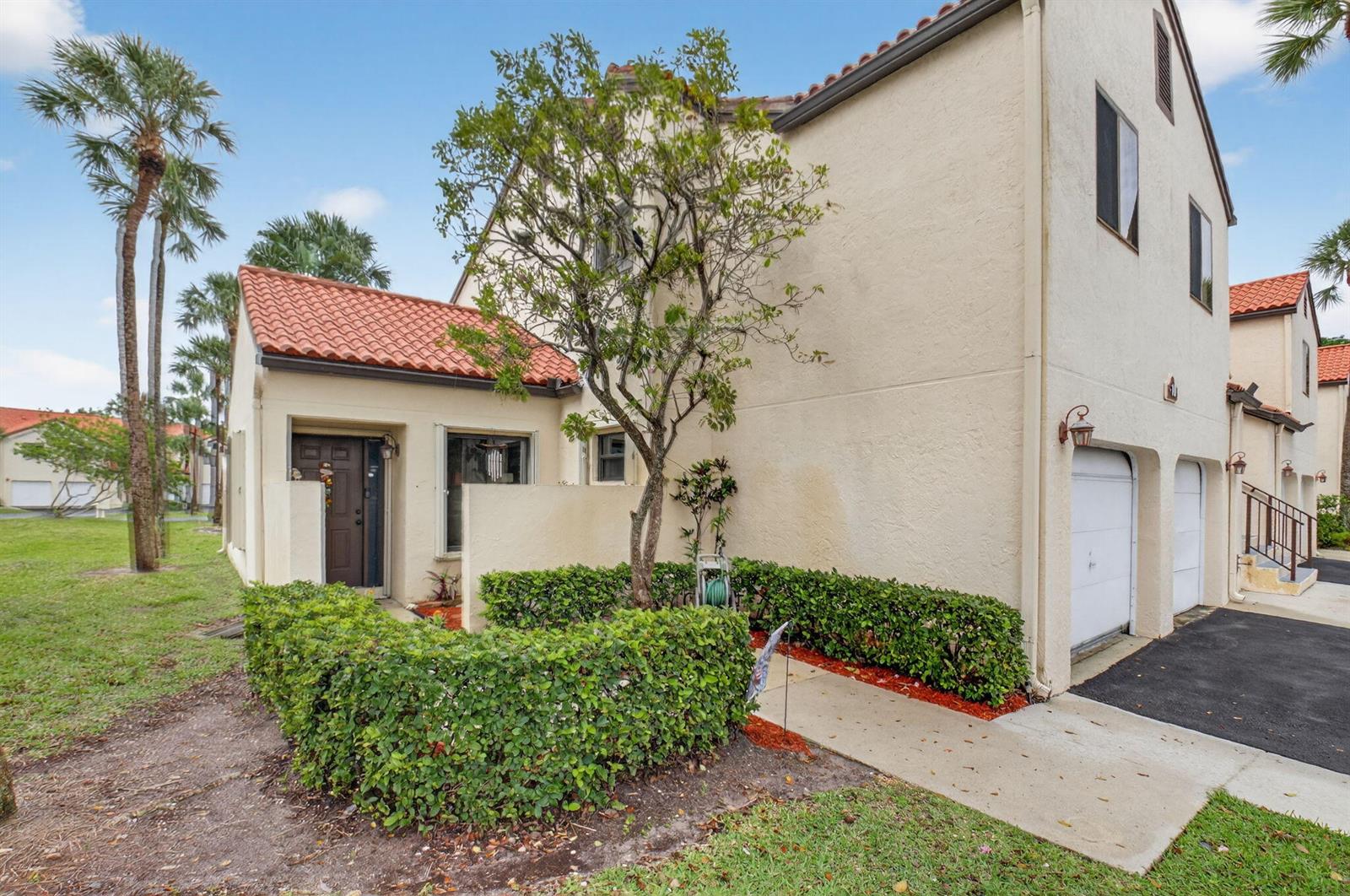 A two-story townhouse with a red tile roof, a small front garden, and a garage — 10 Vía De Casas Sur # 101, Boynton Beach FL 33426, BOYNTON BEACH, FL