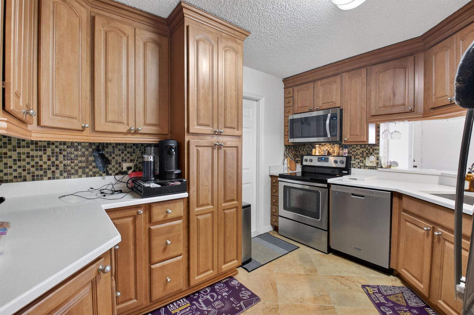 A kitchen features wood cabinets, stainless steel appliances, a mosaic tile backsplash, and tile flooring — 10 Vía De Casas Sur # 101, Boynton Beach FL 33426, BOYNTON BEACH, FL