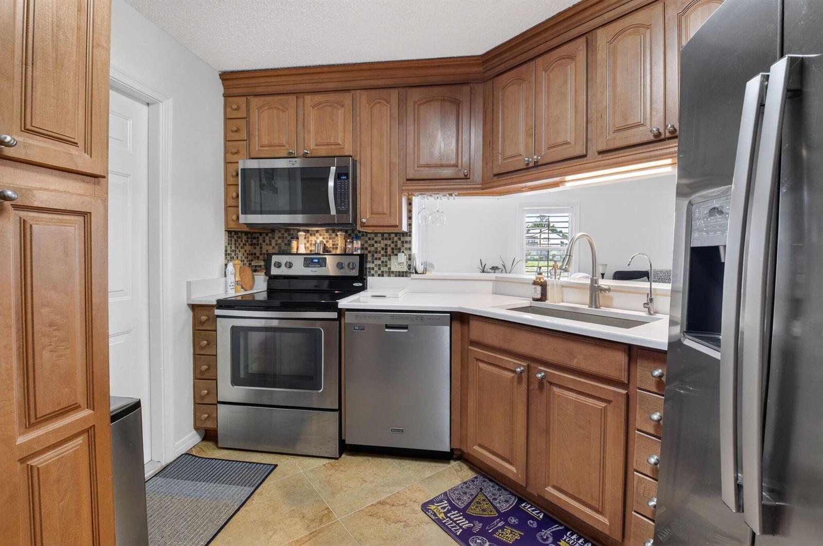 A kitchen features wood cabinets, stainless steel appliances, and a pass-through window to another room — 10 Vía De Casas Sur # 101, Boynton Beach FL 33426, BOYNTON BEACH, FL