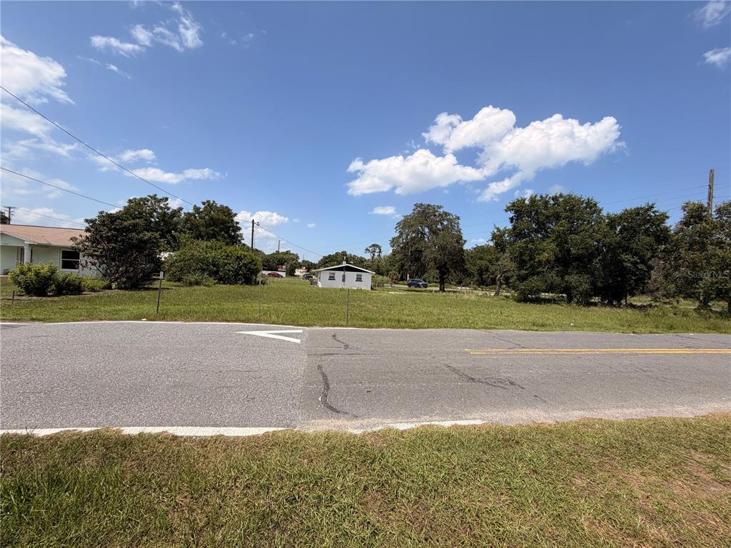 A grassy vacant lot sits next to a small white house along a paved road — HIGHWAY 561 HIGHWAY, TAVARES, FL