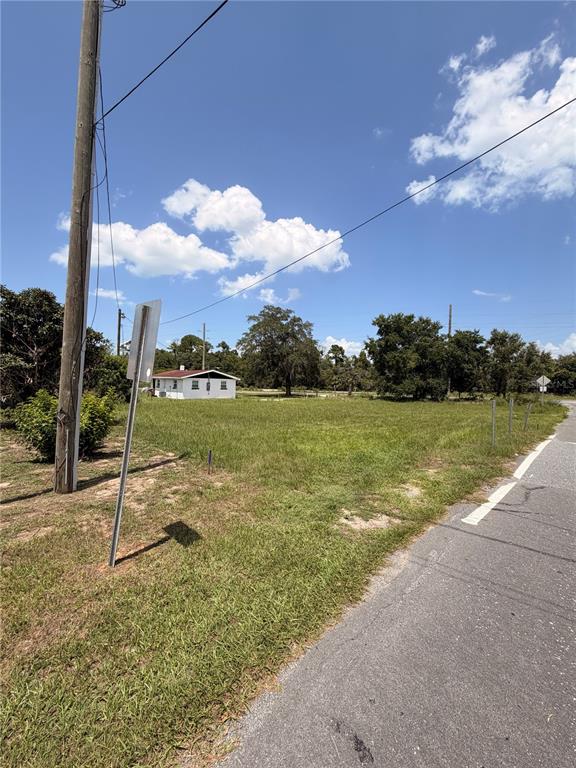 A vacant, grassy lot sits beside a paved road with a small house in the distance — HIGHWAY 561 HIGHWAY, TAVARES, FL