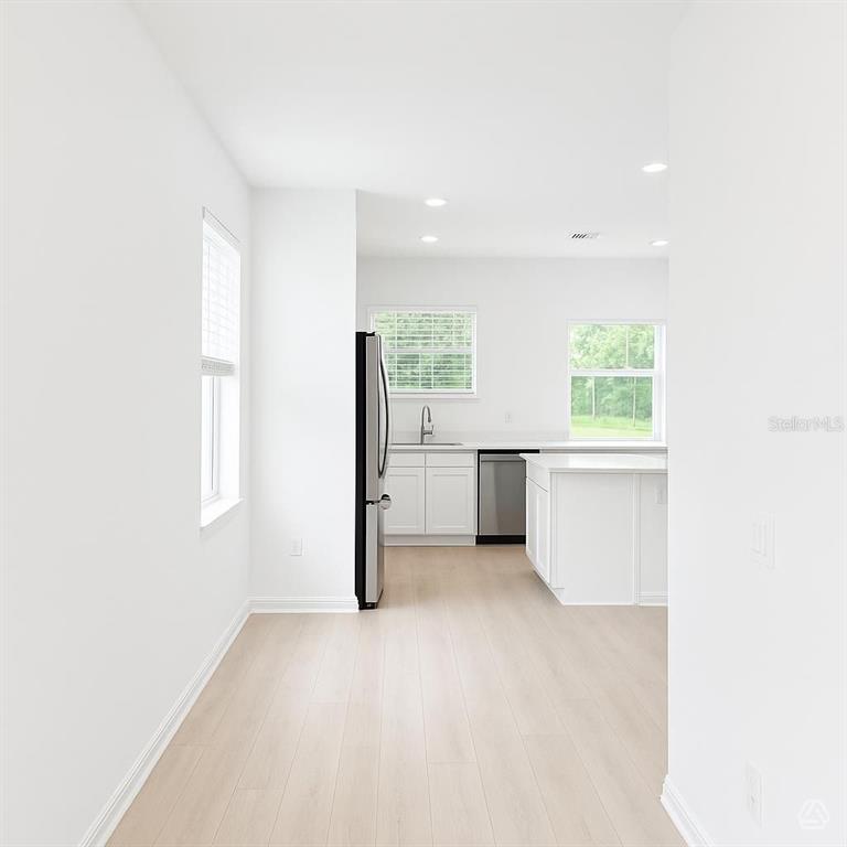 A bright kitchen features white cabinets, stainless steel appliances, an island, and light wood flooring — 13008 SASSAFRAS TRAIL, PARRISH, FL