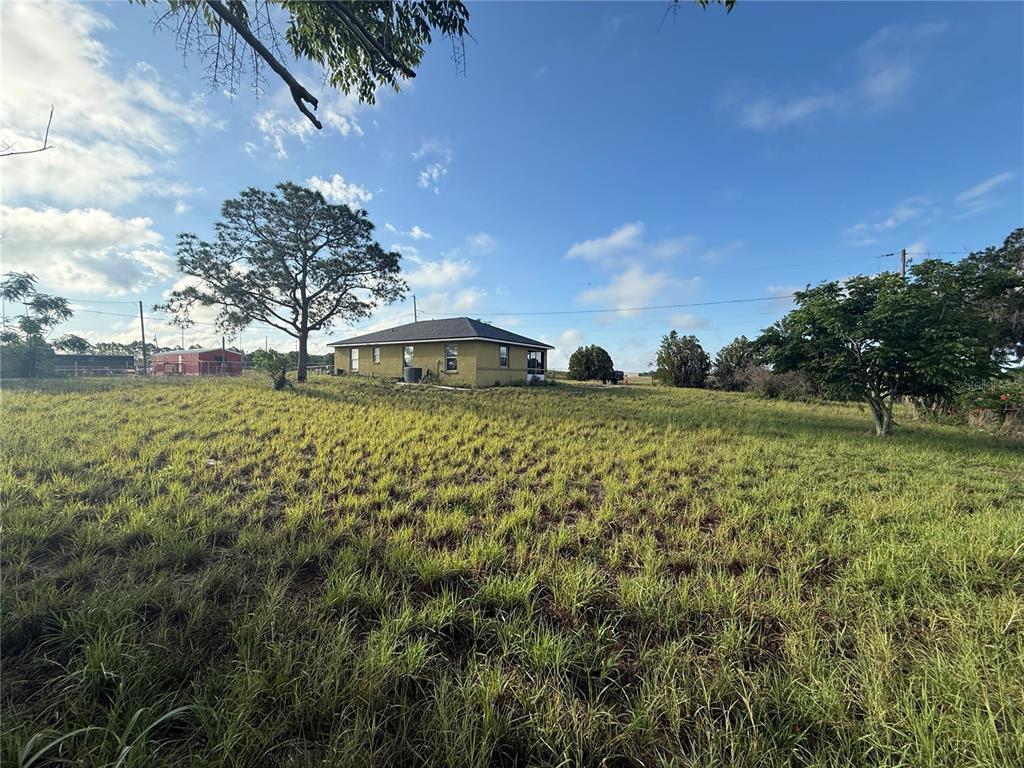 A yellow house sits in a large, grassy field under a bright blue sky — 202 OWENS ROAD, LAKE WALES, FL