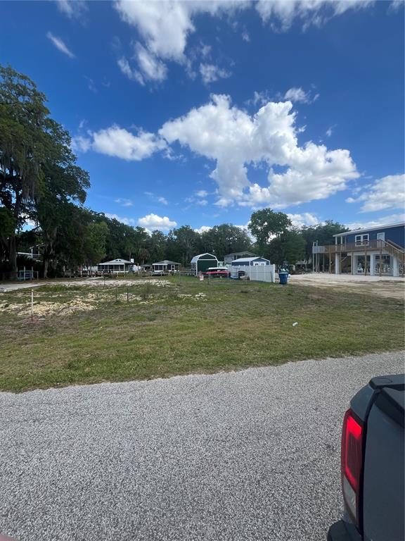 A vacant, grassy lot sits in front of several small houses under a blue sky — 7206 BETHESDA COURT, WEEKI WACHEE, FL