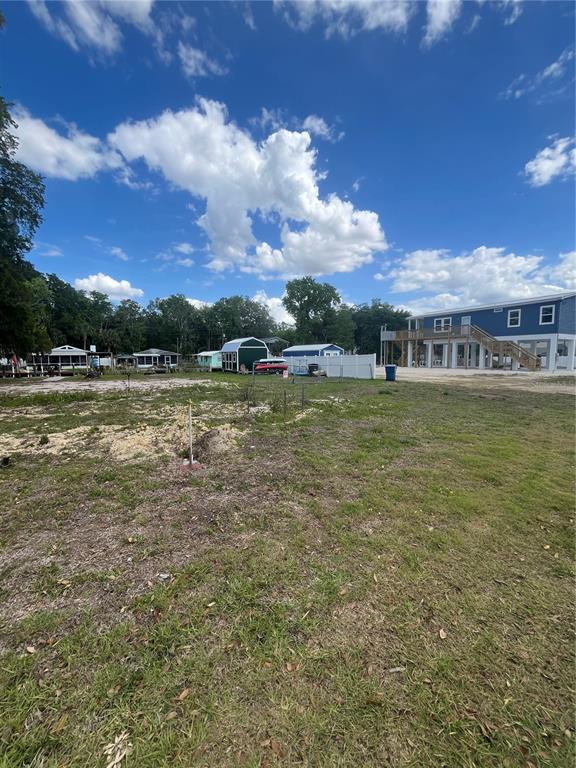 A vacant, grassy lot with a blue elevated house and several small sheds in the background — 7206 BETHESDA COURT, WEEKI WACHEE, FL