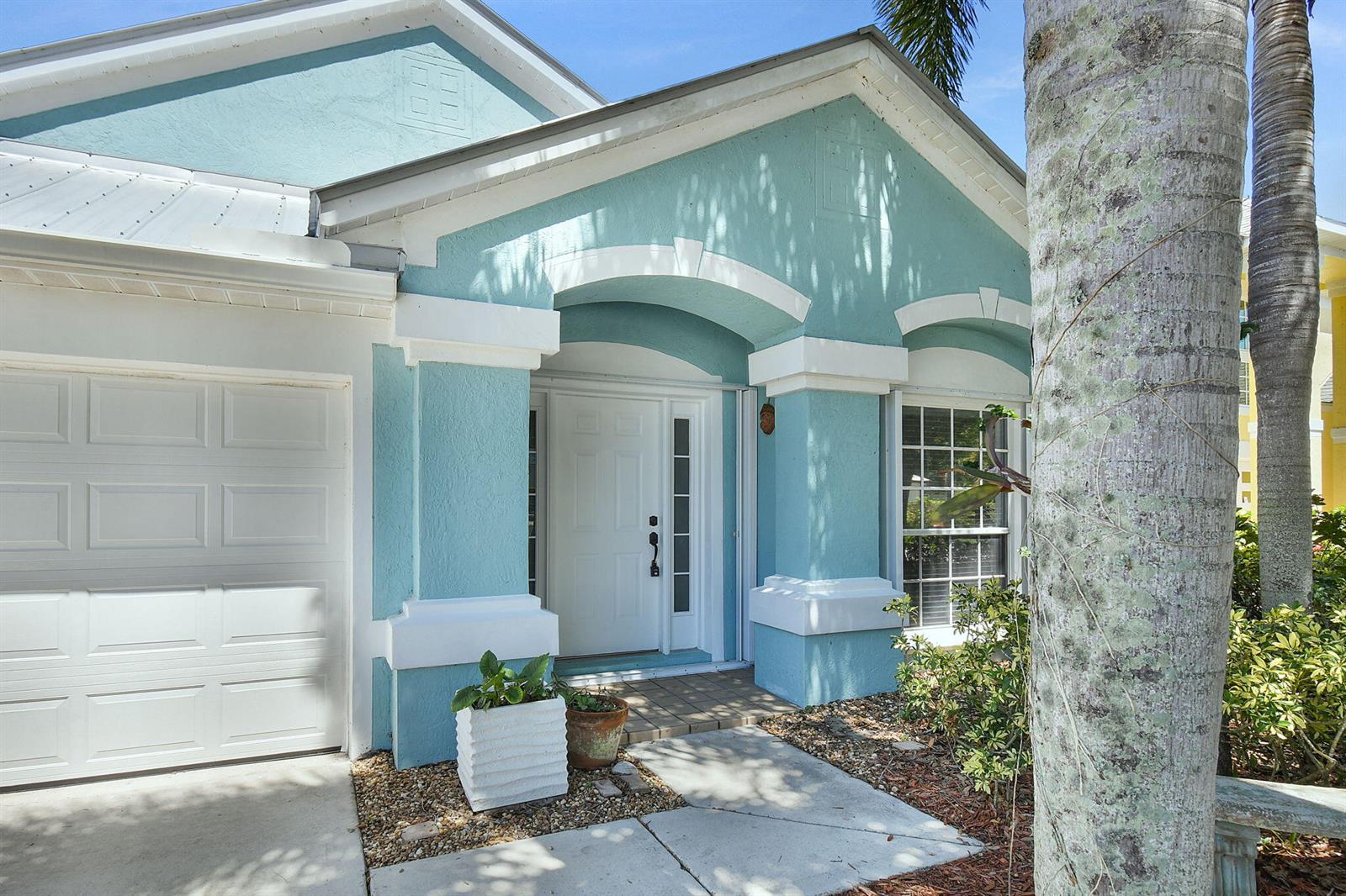 A light blue house exterior features a white front door, garage, and a palm tree — 1959 NW Marsh Rabbit Lane, Jensen Beach FL 34957, JENSEN BEACH, FL
