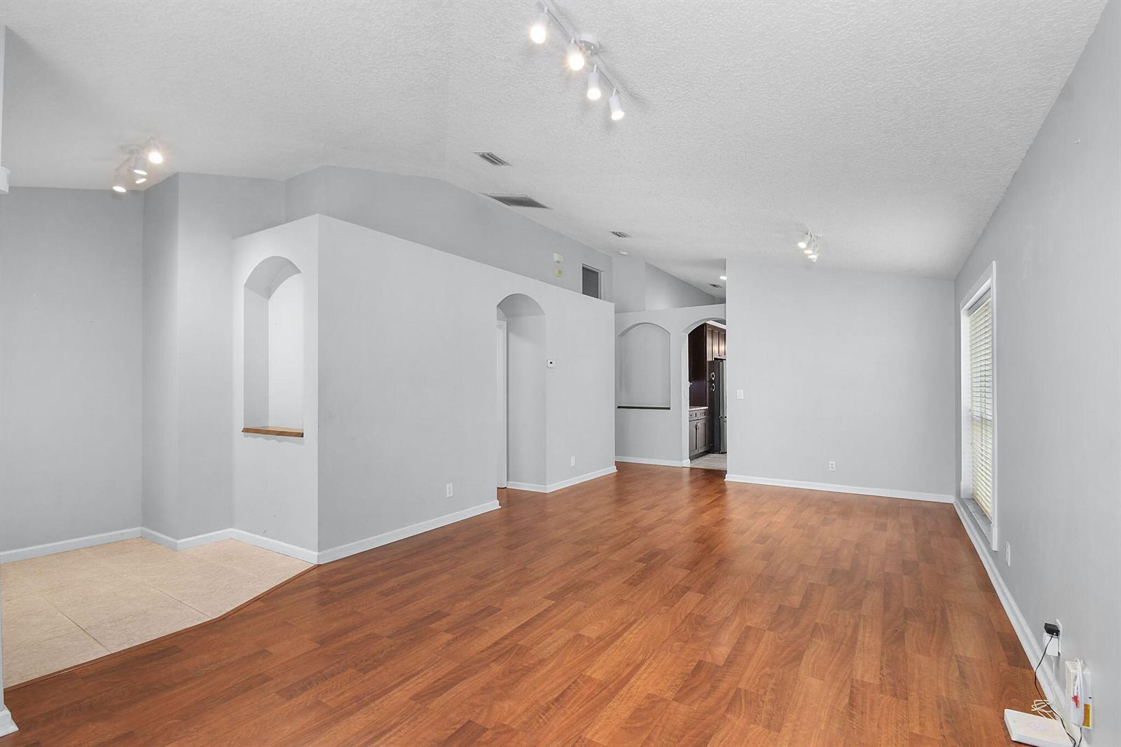 An empty living room features light gray walls, wood-look flooring, and recessed arched wall niches — 1959 NW Marsh Rabbit Lane, Jensen Beach FL 34957, JENSEN BEACH, FL