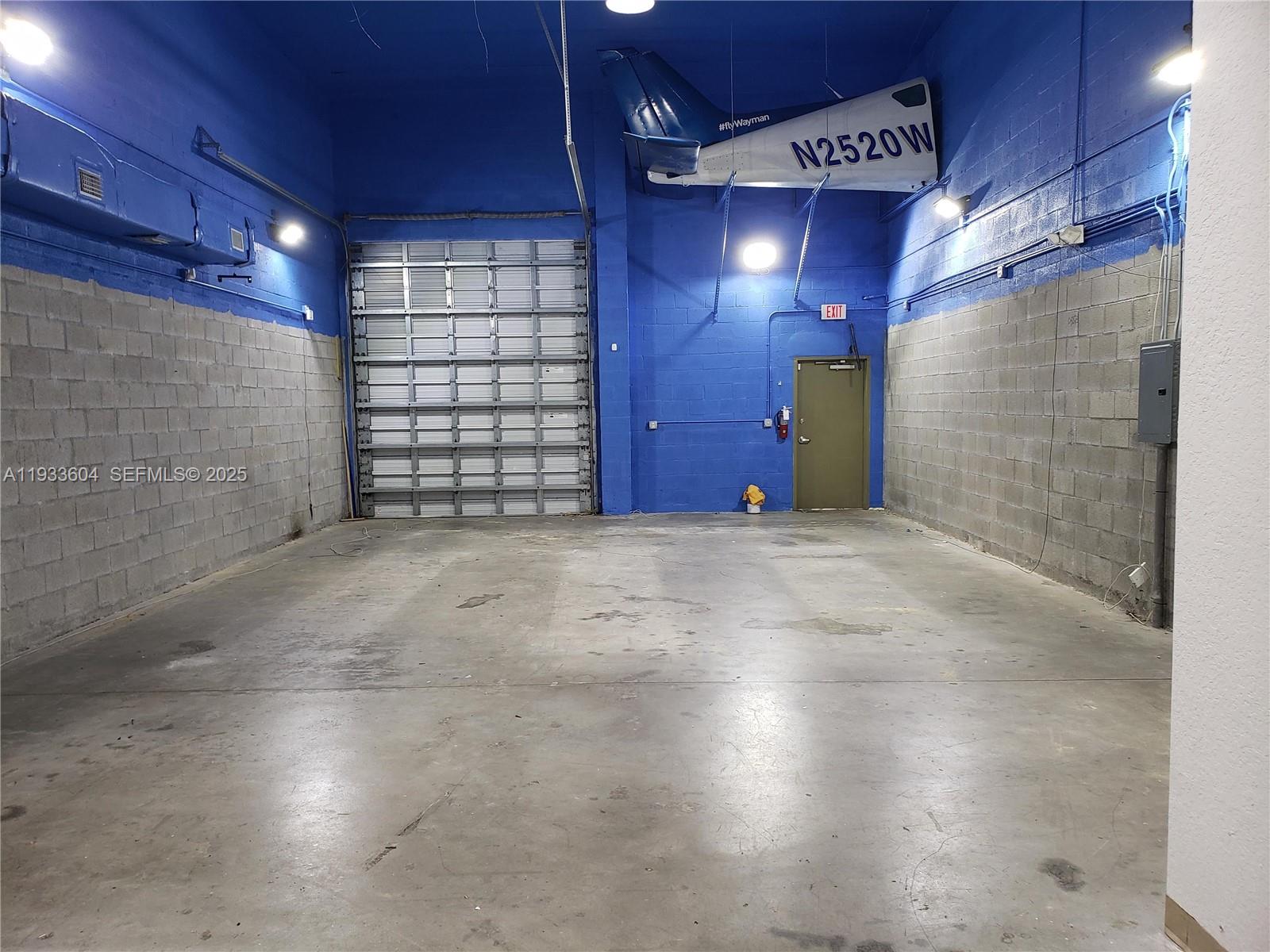 An industrial warehouse space features blue walls, a concrete floor, and an airplane tail mounted overhead — 13491 NW 47th Ave # 2, Opa-Locka FL 33054, OPA-LOCKA, FL