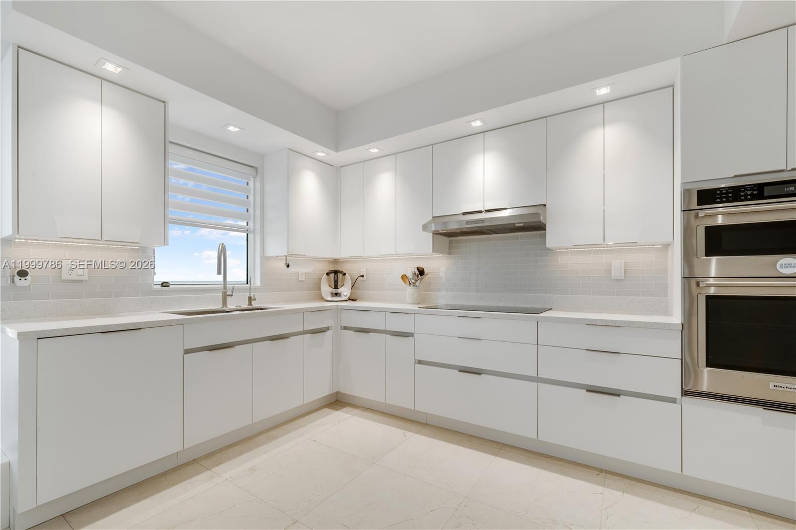 A modern white kitchen features flat-panel cabinetry, stainless steel appliances, and light-colored tile flooring — 789 Crandon Blvd # 1003, Key Biscayne FL 33149, KEY BISCAYNE, FL