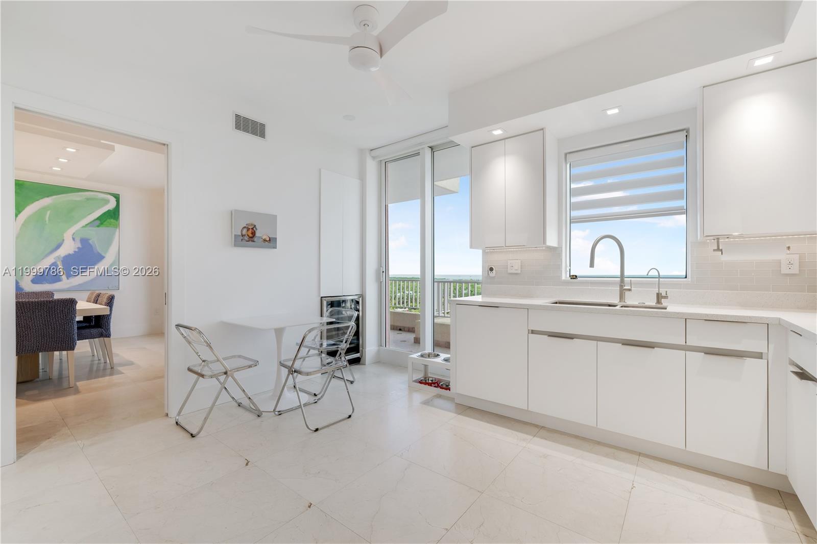 A bright, modern white kitchen features a small dining area and a balcony view — 789 Crandon Blvd # 1003, Key Biscayne FL 33149, KEY BISCAYNE, FL