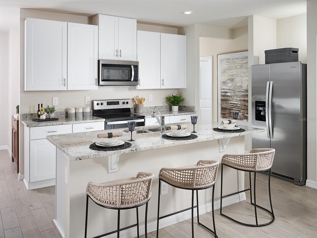 A kitchen features white cabinets, granite countertops, stainless steel appliances, and a breakfast bar with stools — 3902 TEAK LANE, BARTOW, FL