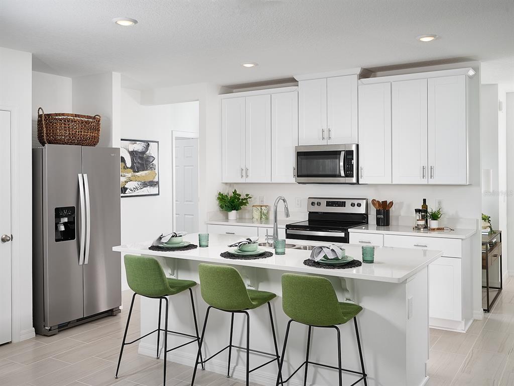 A modern kitchen features white cabinetry, stainless steel appliances, a quartz island, and green stools — 3902 TEAK LANE, BARTOW, FL