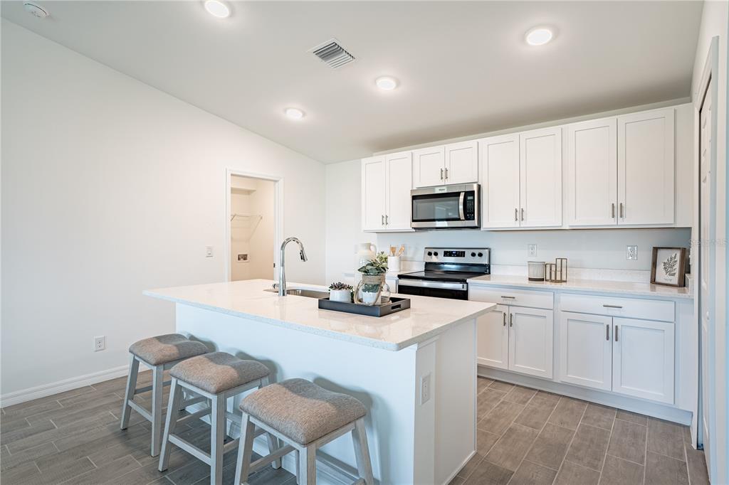 A modern kitchen features white cabinets, quartz countertops, a center island with stools, and tile flooring — 21035 NOWELL AVENUE, PORT CHARLOTTE, FL