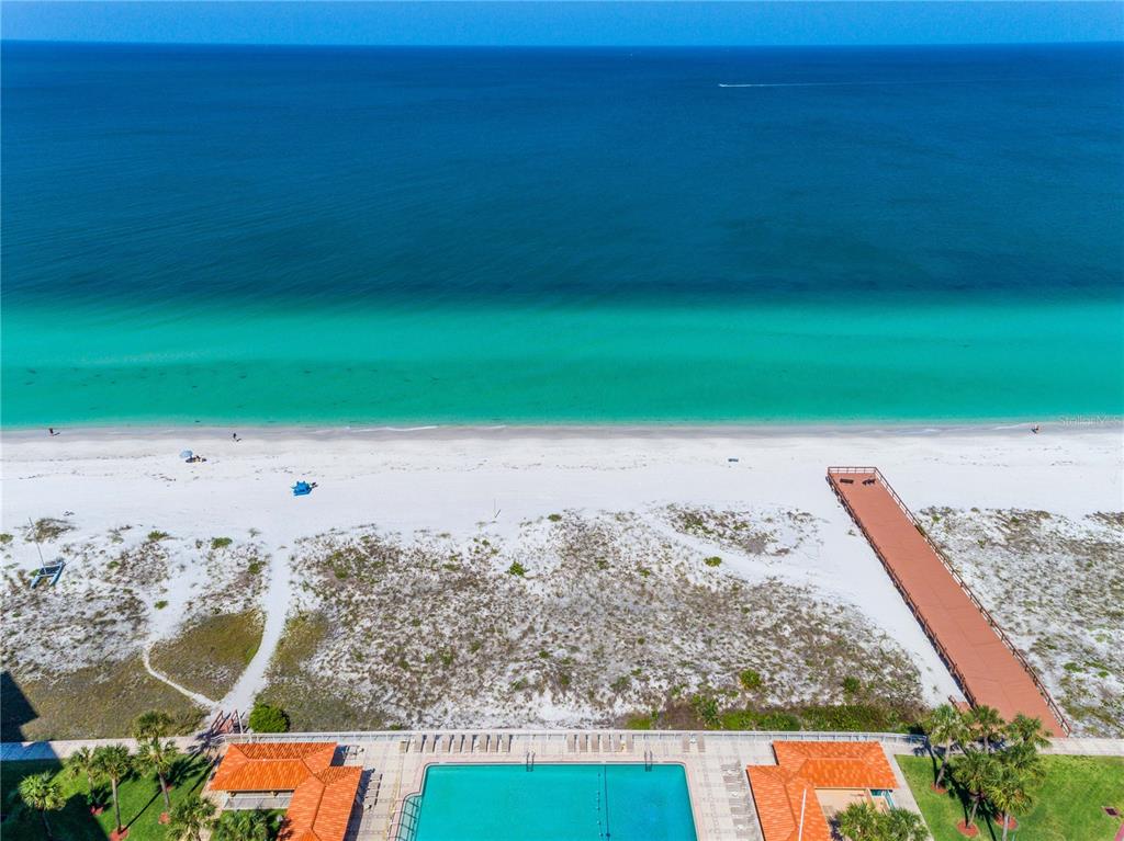 An aerial view shows a swimming pool, a wooden boardwalk, white sand, and the ocean — 880 MANDALAY AVENUE UNIT S103, CLEARWATER, FL