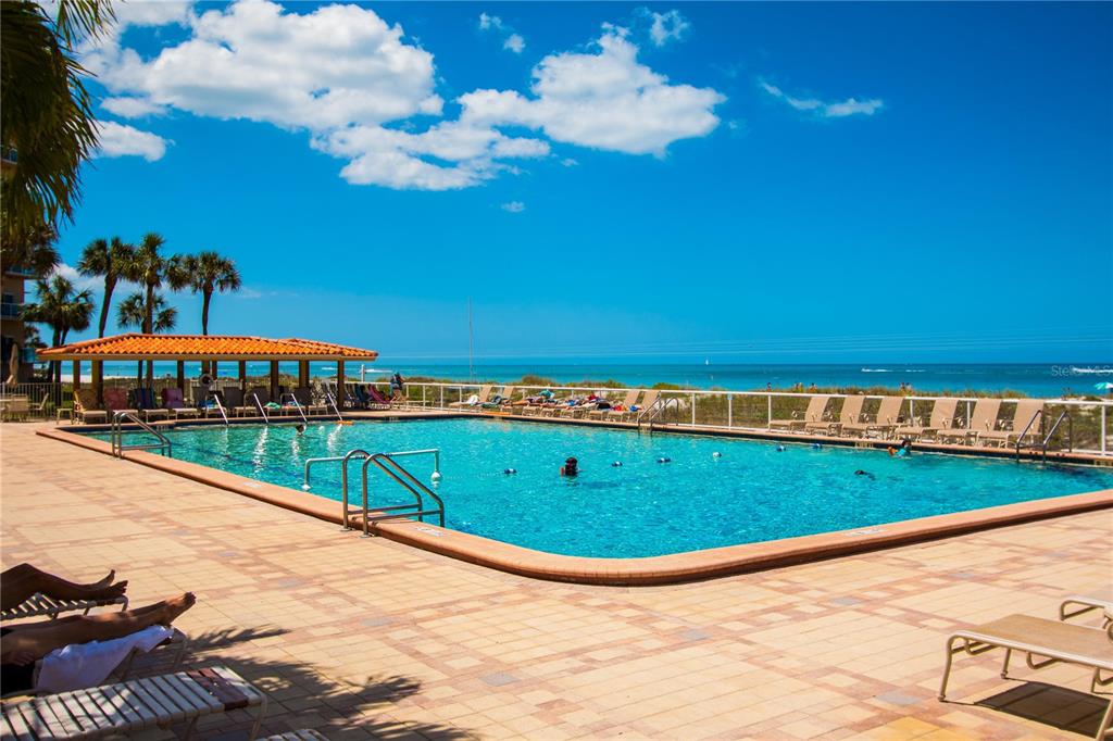 A swimming pool sits on a patio overlooking the ocean with palm trees and lounge chairs — 880 MANDALAY AVENUE UNIT S103, CLEARWATER, FL