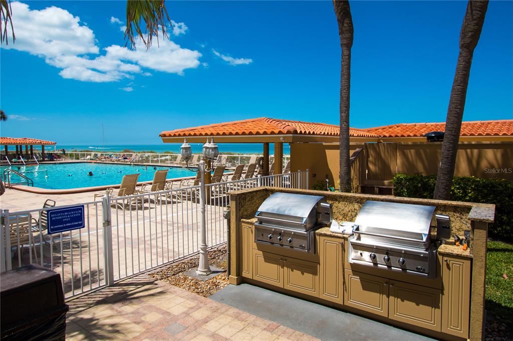 An outdoor kitchen with two stainless steel grills sits beside a swimming pool and ocean — 880 MANDALAY AVENUE UNIT S103, CLEARWATER, FL