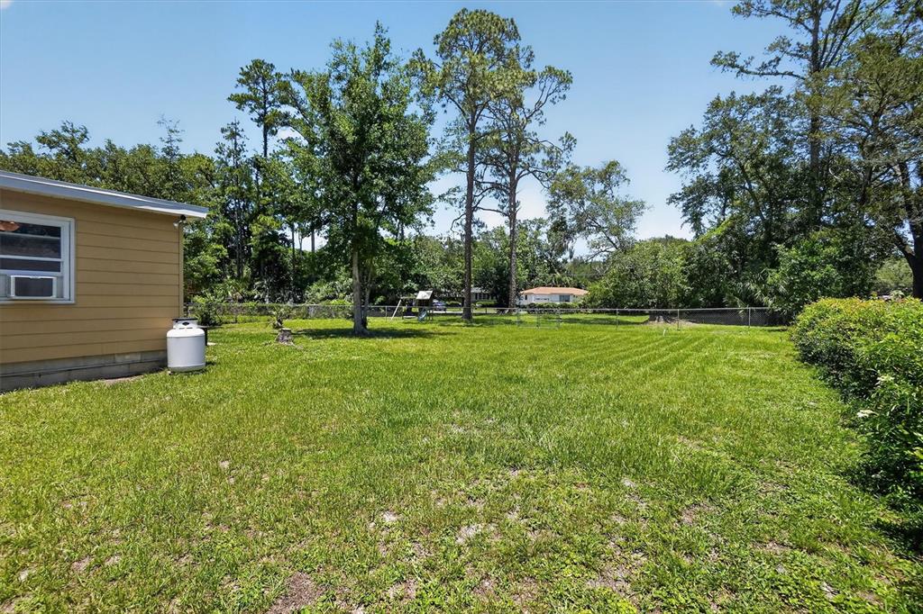 A grassy backyard features a yellow house exterior, a propane tank, and mature trees — 5503 LAKEWOOD CIRCLE E, JACKSONVILLE, FL