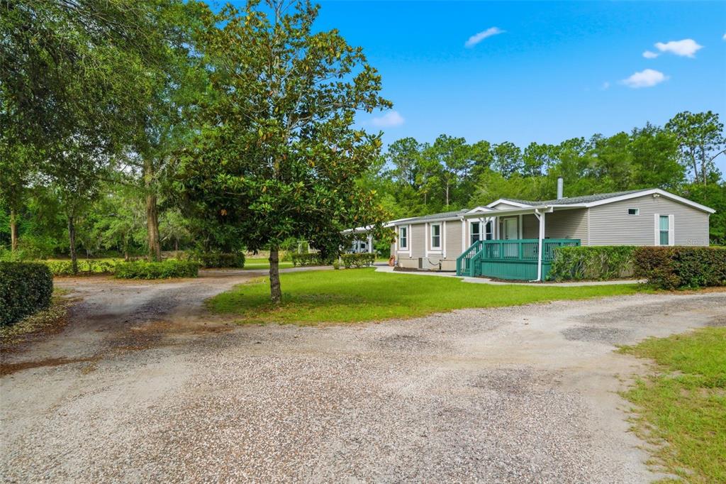 A single-story manufactured home with a green deck sits on a gravel lot with trees — 2564 N CREDE AVENUE, CRYSTAL RIVER, FL