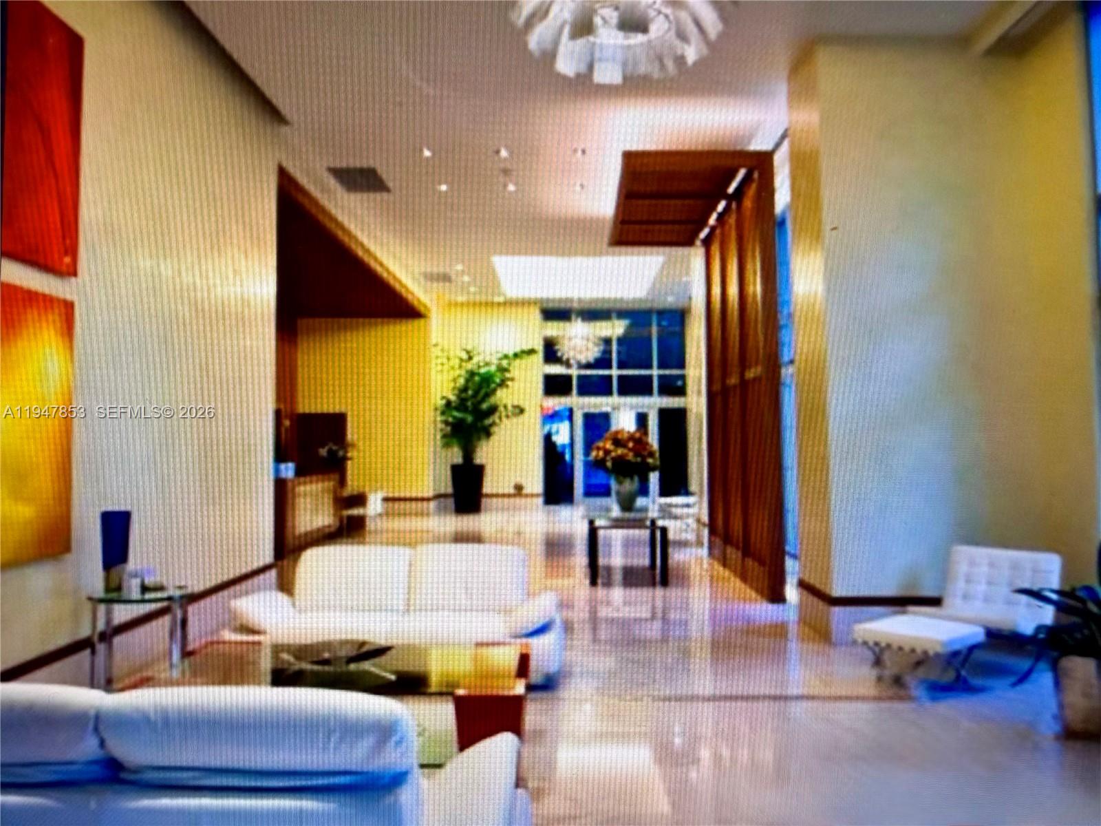 A modern building lobby features white sofas, marble floors, and decorative wood paneling — 1050 Brickell Ave # 1816, Miami FL 33131, MIAMI, FL