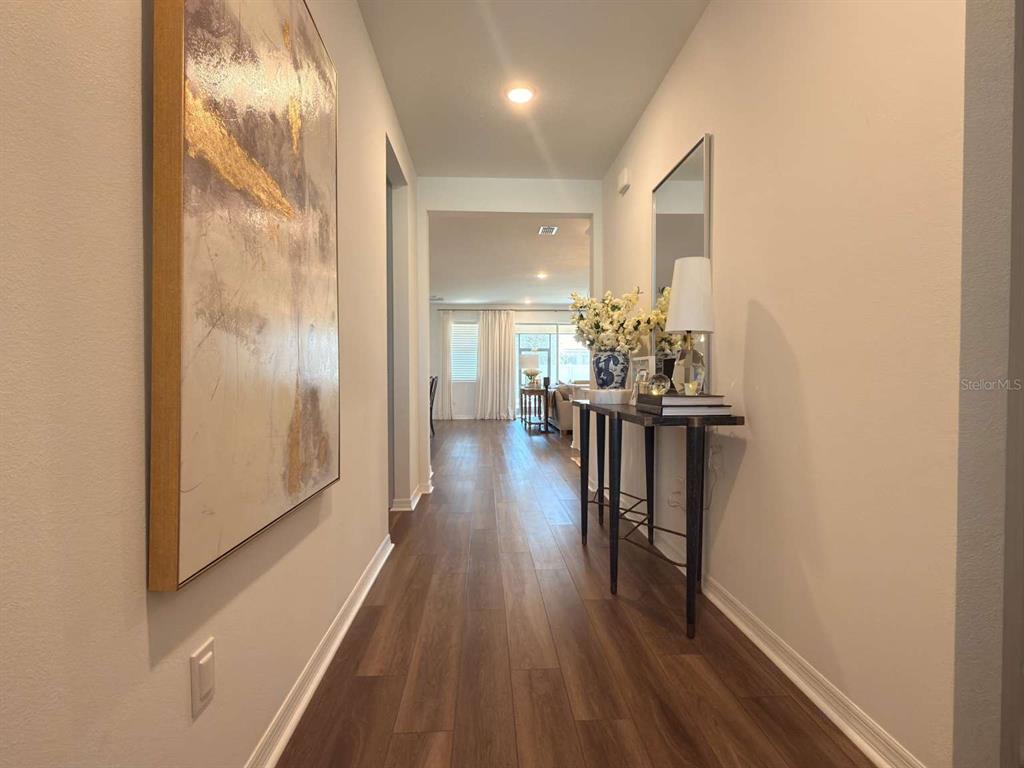 A hallway with wood-look flooring, a large abstract painting, and a console table with decor — 3081 AMBERSWEET PLACE, CLERMONT, FL