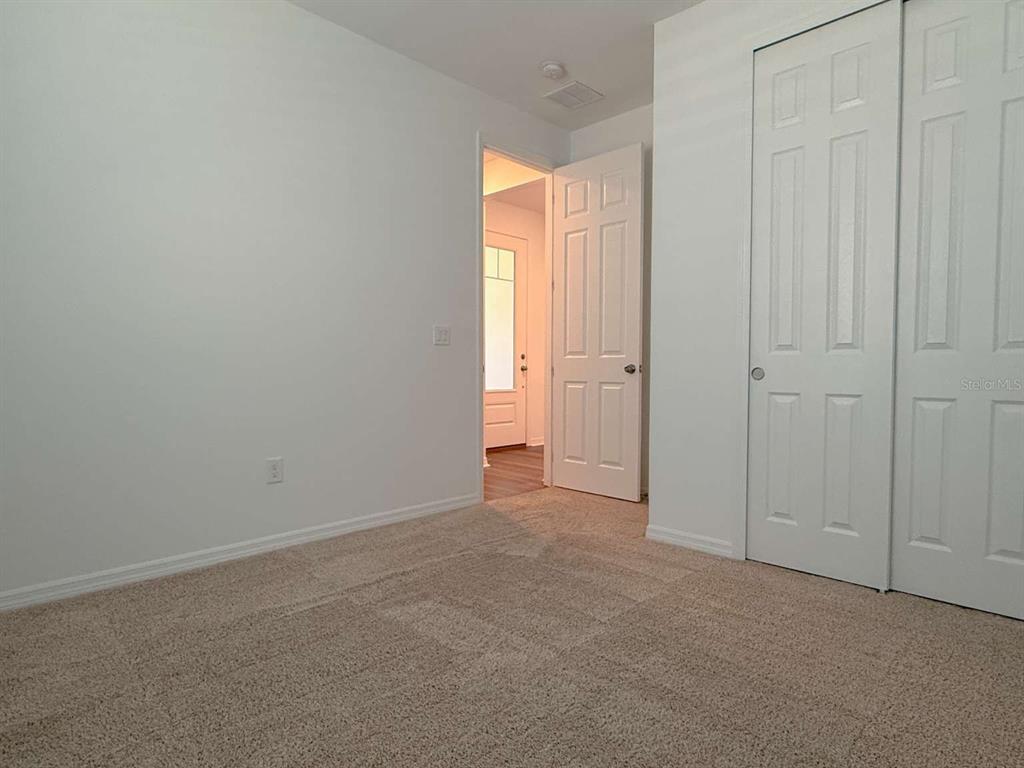 A carpeted bedroom features white walls, a closet with double doors, and an open doorway — 3081 AMBERSWEET PLACE, CLERMONT, FL