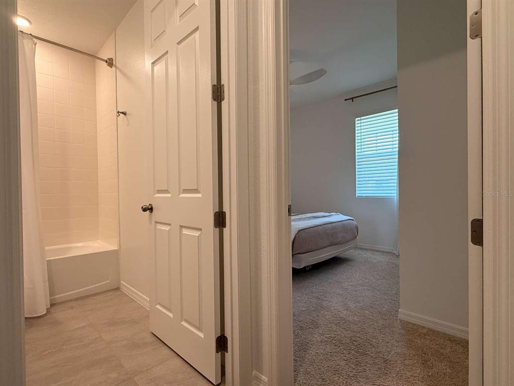 A bathroom with a tub-shower combo sits next to an open doorway into a bedroom — 3081 AMBERSWEET PLACE, CLERMONT, FL
