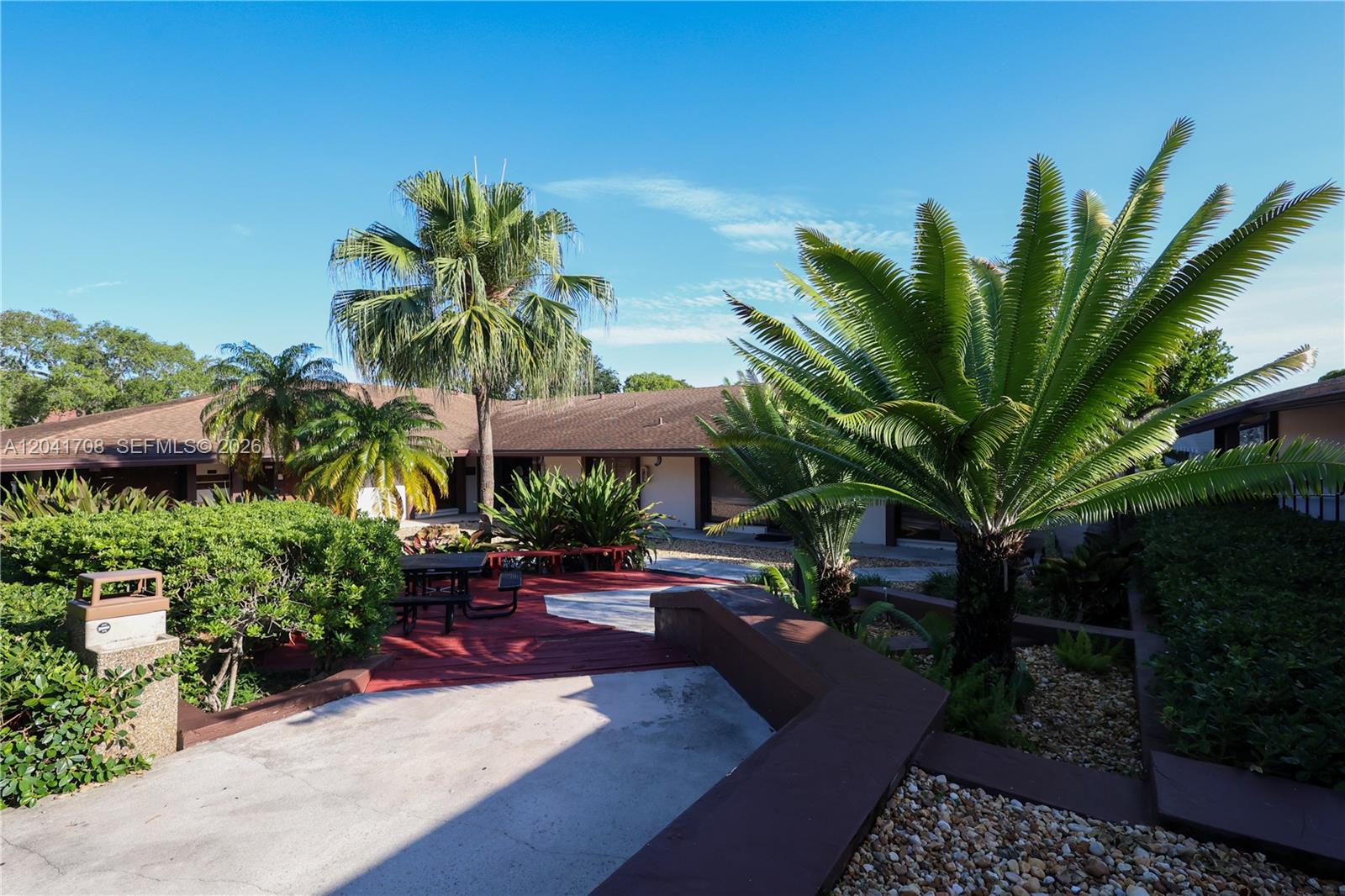 A paved walkway leads to a red wooden deck with a table in front of a building — 8525 SW 92nd St # 11B, Miami FL 33156, MIAMI, FL