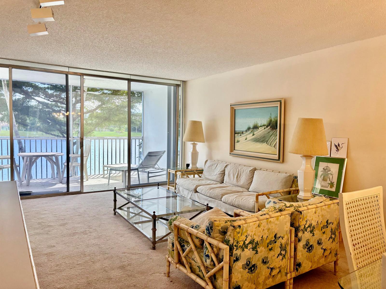 A living room with bamboo-style furniture, a glass coffee table, and a balcony overlooking water — 3150 N Course Lane # 202, Pompano Beach FL 33069, POMPANO BEACH, FL