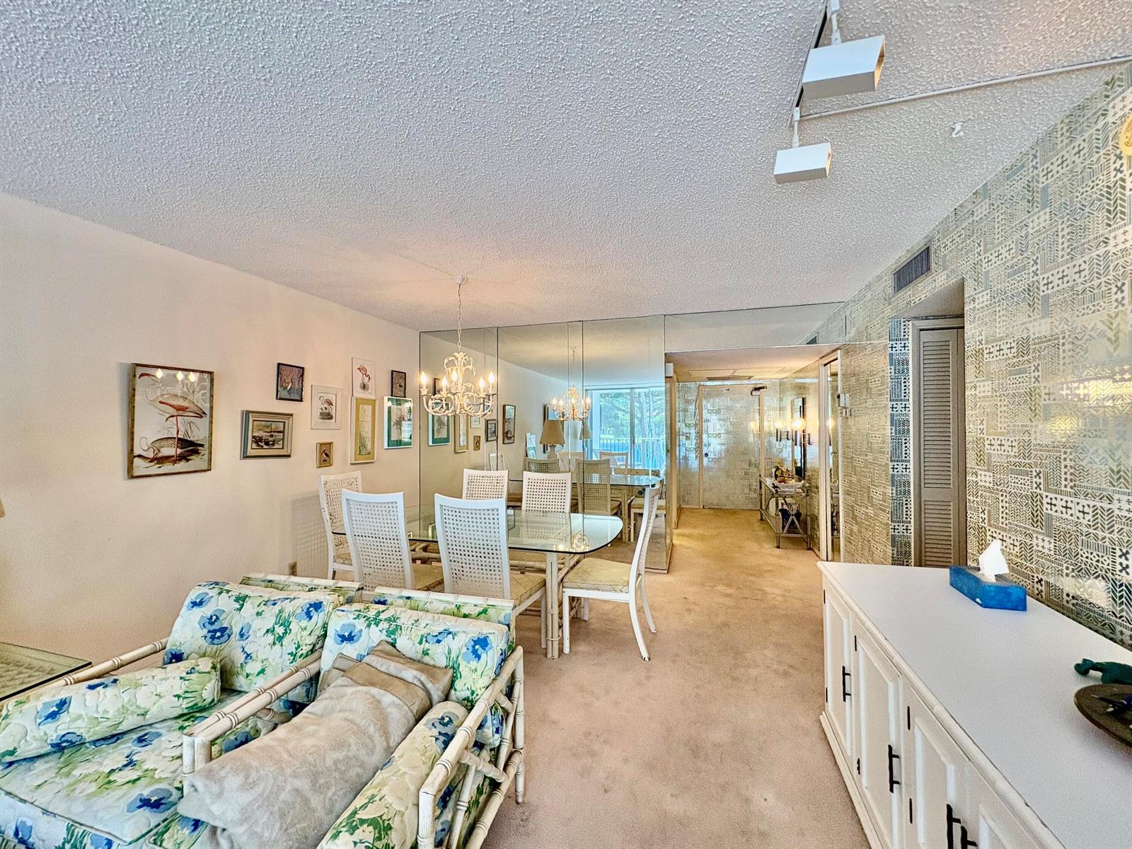 A dining area with a glass table, white chairs, and mirrored walls next to a living space — 3150 N Course Lane # 202, Pompano Beach FL 33069, POMPANO BEACH, FL