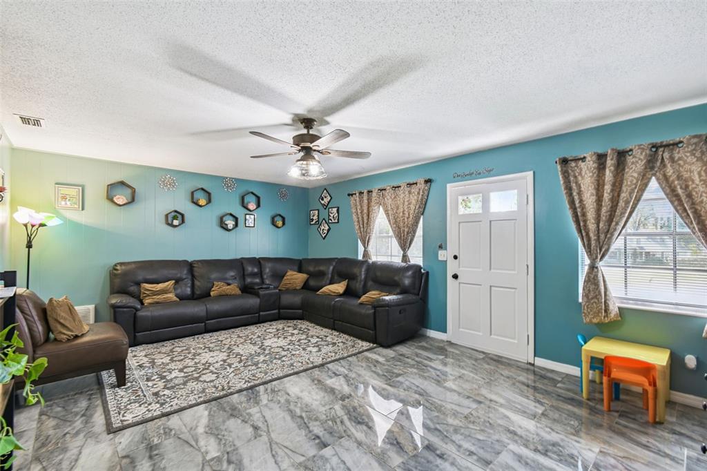 A living room features a large sectional sofa, teal walls, and marble-look tile flooring — 25309 CARNOUSTIE DRIVE, SORRENTO, FL