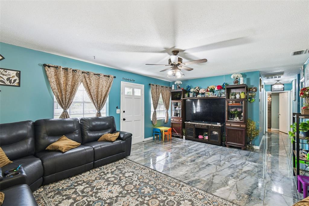 A living room features teal walls, a dark leather sectional, and gray marble-look tile flooring — 25309 CARNOUSTIE DRIVE, SORRENTO, FL