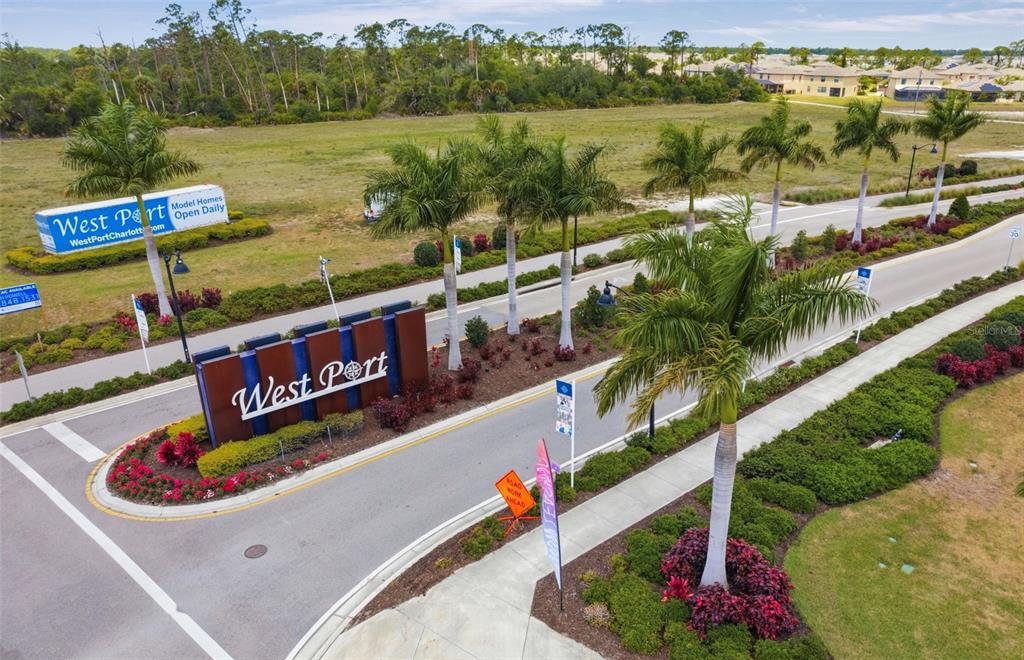 An aerial view shows the entrance sign and landscaped road leading into the West Port community — 1921 E ISLES ROAD, PORT CHARLOTTE, FL