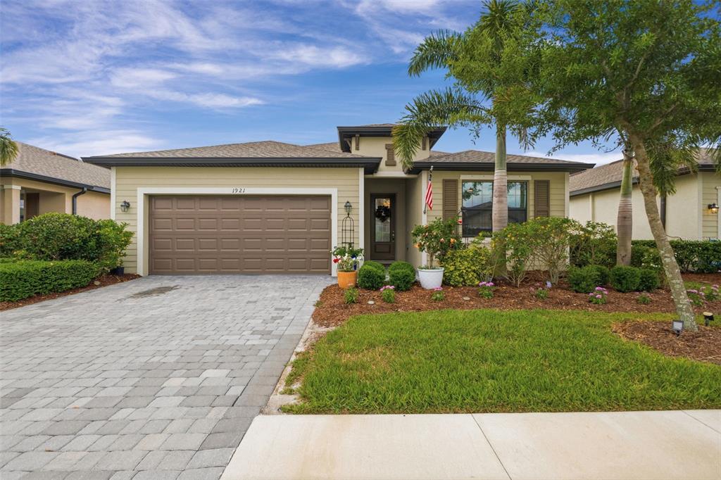 A single-story house with a paved driveway, brown garage door, and palm trees in front — 1921 E ISLES ROAD, PORT CHARLOTTE, FL