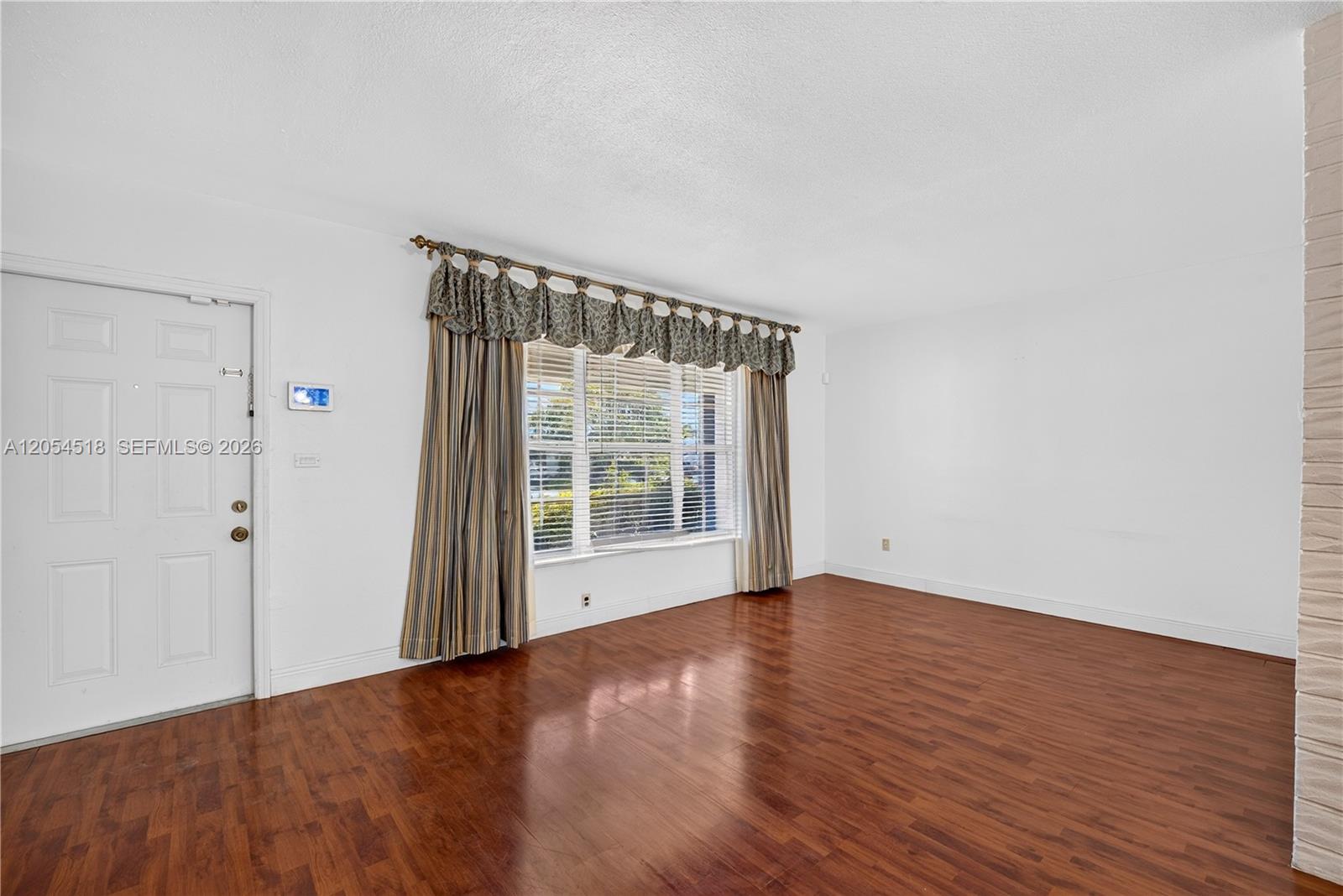 A living room features white walls, dark wood flooring, and a window with patterned curtains — 12021 SW 174th St, Miami FL 33177, MIAMI, FL