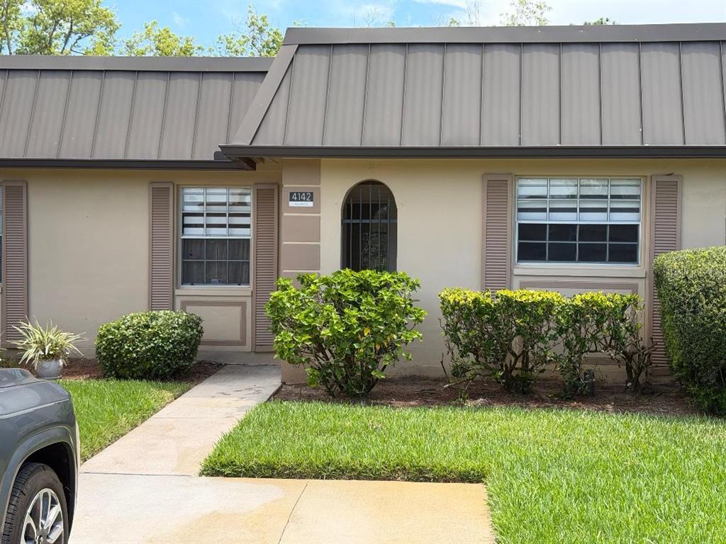 A single-story residential building exterior with a metal roof, arched entryway, and landscaped front yard — 4142 HAMPTON DRIVE UNIT 4142, NEW PORT RICHEY, FL