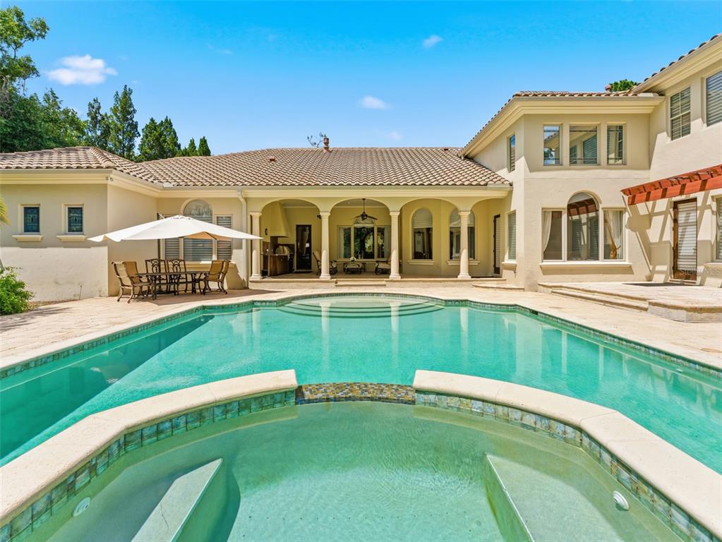 A backyard swimming pool and hot tub sit in front of a two-story stucco house — 18901 LAKES EDGE WAY, ODESSA, FL