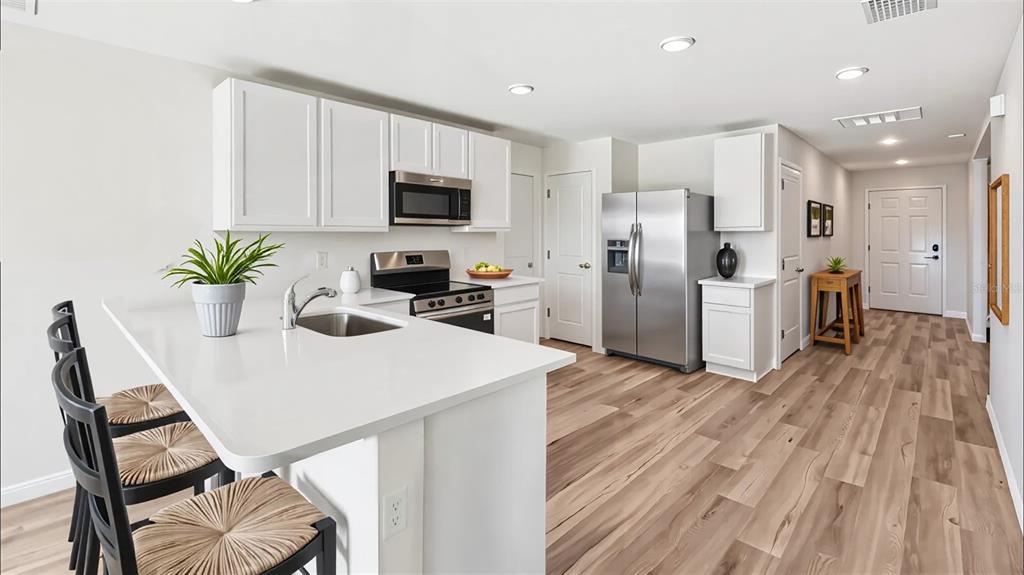 A modern kitchen features white cabinetry, stainless steel appliances, a quartz island, and wood flooring — 2239 W MENORES DRIVE, DUNNELLON, FL