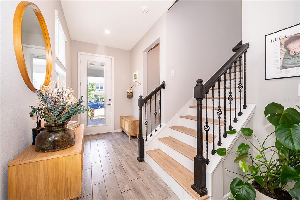An entryway features wood-look tile flooring, a staircase with black railings, and a round mirror — 14226 LANIKAI BEACH DRIVE, ORLANDO, FL
