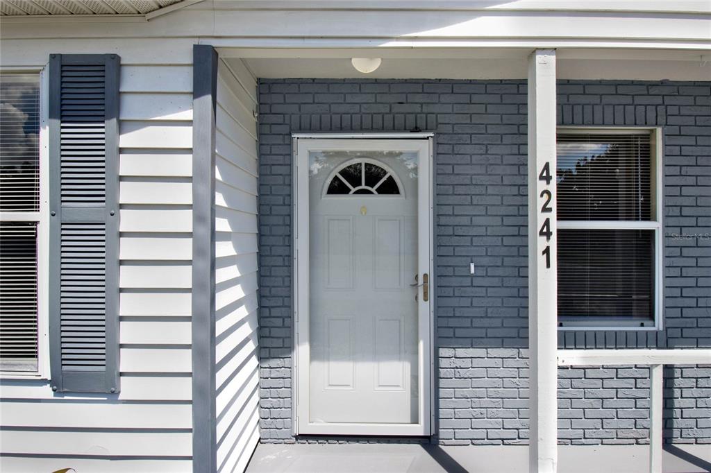 A white front door with a glass arch sits between gray brick walls and siding — 4241 ALAMANDA BOULEVARD, LAKE WALES, FL