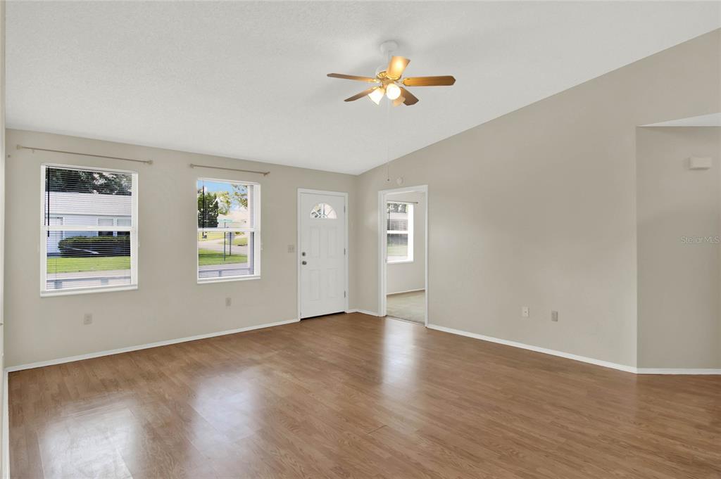 An empty living room features light-colored walls, wood-look flooring, a ceiling fan, and two windows — 4241 ALAMANDA BOULEVARD, LAKE WALES, FL