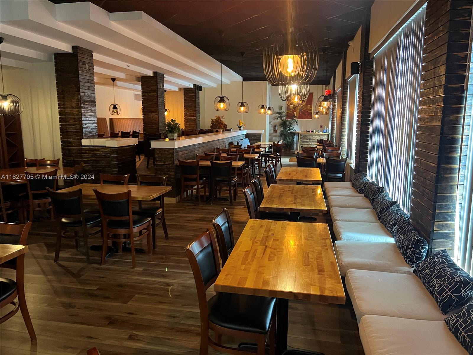 A restaurant interior features wooden tables, dark chairs, booth seating, and hanging pendant lights — 148 NW 167th St, Miami FL 33169, MIAMI, FL