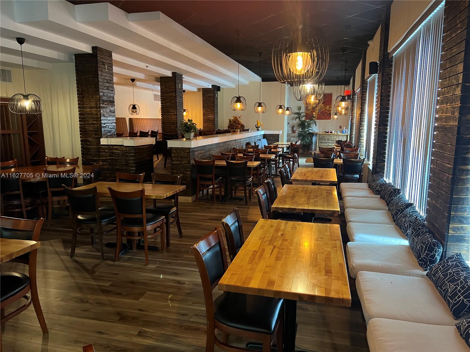 A restaurant interior features wooden tables, black chairs, booth seating, and hanging pendant lights — 148 NW 167th St, Miami FL 33169, MIAMI, FL
