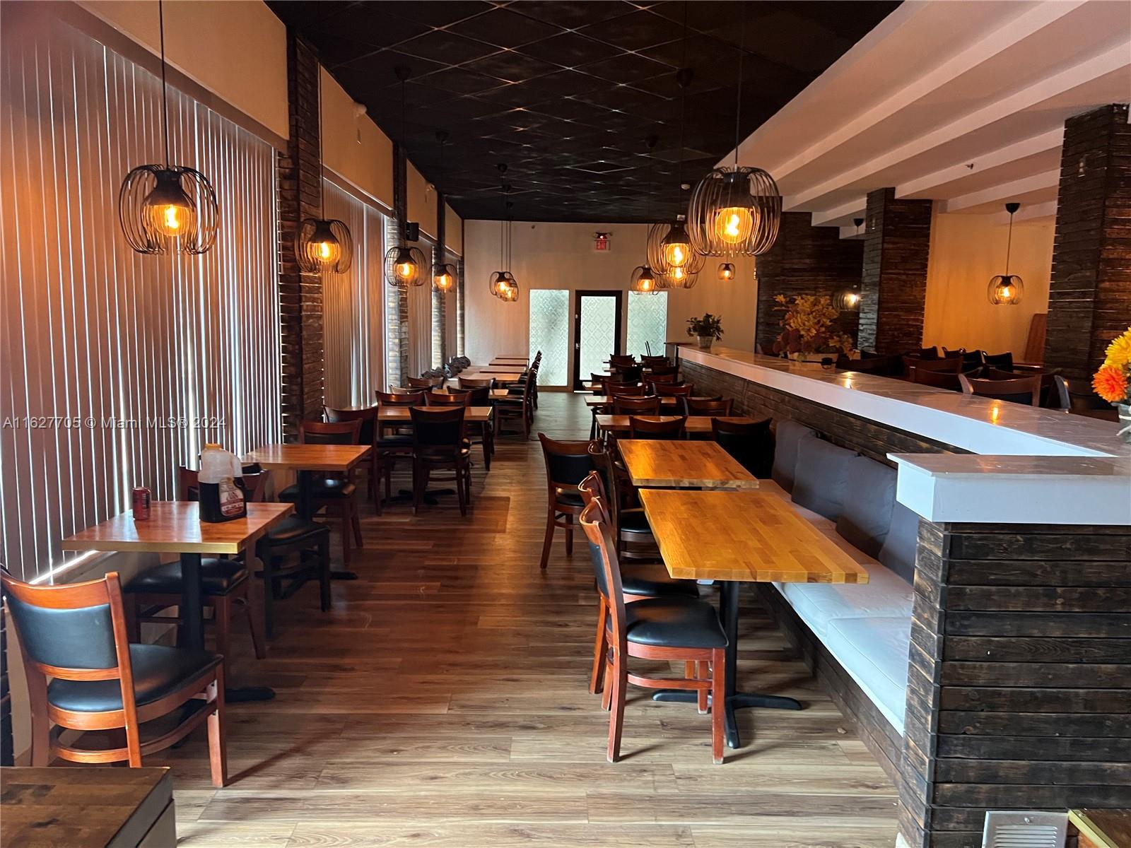 A restaurant interior features wooden tables, black chairs, pendant lighting, and a long booth — 148 NW 167th St, Miami FL 33169, MIAMI, FL