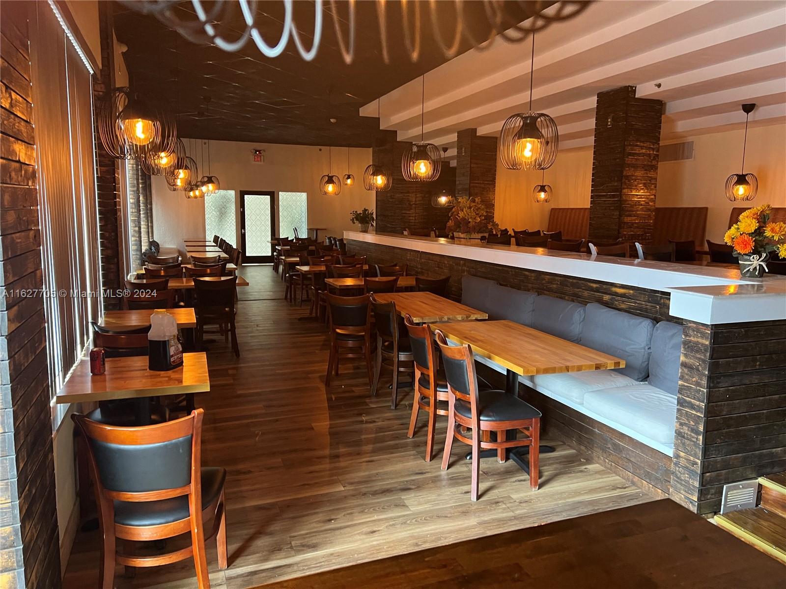 A restaurant interior features wooden tables, chairs, booth seating, and hanging pendant lights — 148 NW 167th St, Miami FL 33169, MIAMI, FL