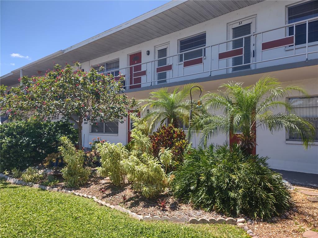 A two-story apartment building exterior with a balcony, red doors, and landscaped front yard — 5850 18TH STREET N UNIT 23, ST PETERSBURG, FL