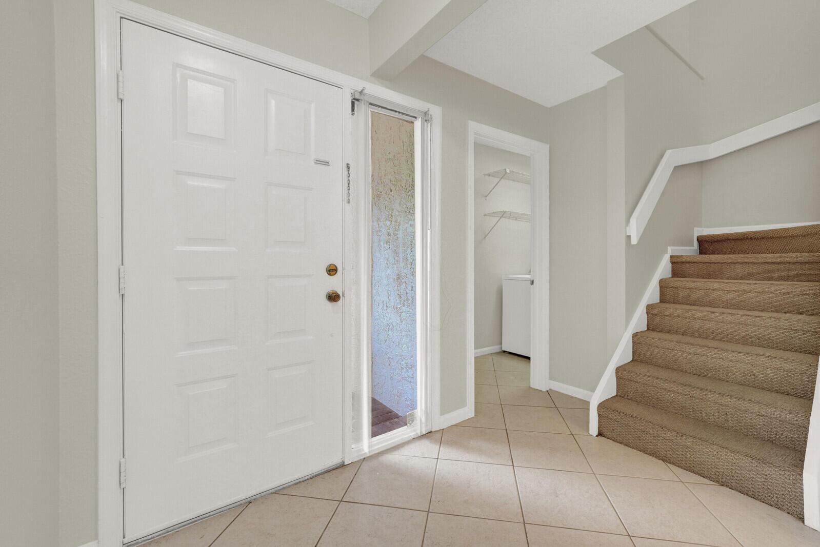 An entryway features a white front door, tiled flooring, a small laundry closet, and carpeted stairs — 6371 Toulon Drive, Boca Raton FL 33433, BOCA RATON, FL