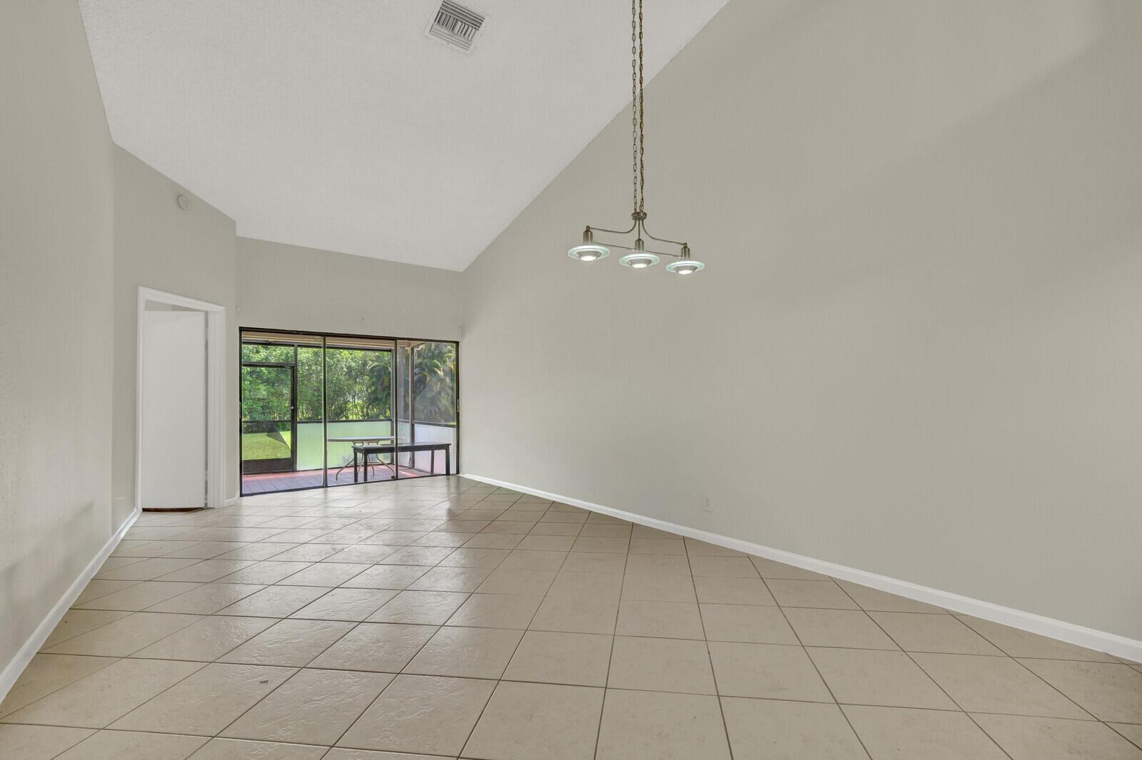 An empty room with beige tile flooring, a vaulted ceiling, and a sliding glass door — 6371 Toulon Drive, Boca Raton FL 33433, BOCA RATON, FL