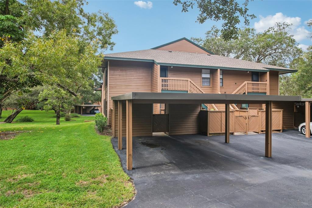 A two-story brown wood-sided building features a covered carport and a grassy lawn area — 2407 CYPRESS POND ROAD UNIT 2407, PALM HARBOR, FL